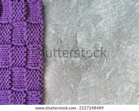 Piece of purple knitted fabric on gray background with copy space. Knitted chess pattern and texture close up. Handmade and needlework hobbies. 