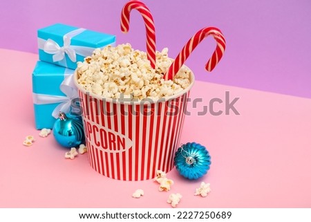 Bucket of popcorn with candy canes, Christmas balls and presents on color background