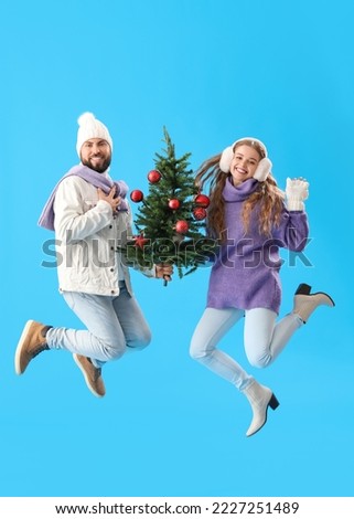 Young couple with Christmas tree jumping on blue background