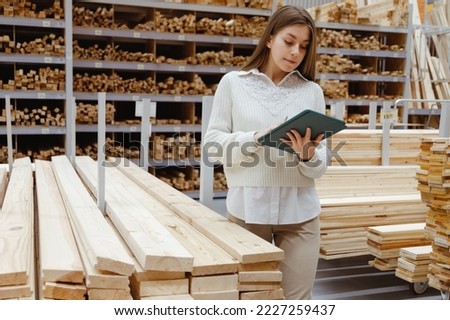Woman with tablet in a timber and lumber warehouse or hardware store. Product acceptance and quality control. Worker woman expert and storekeeper. Royalty-Free Stock Photo #2227259437