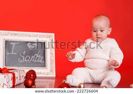 Cute baby sitting on floor with sign I love Santa, christmas presents and decorations over red