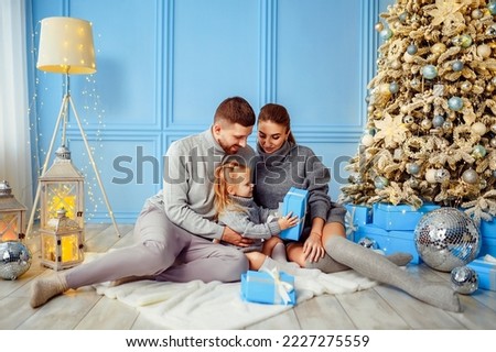 Happy family little cute girl, mather and father opening gift box near Christmas tree in living room. Christmas concept. New Year 