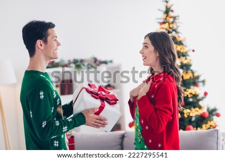 Photo picture of excited young couple lady wear ugly red sweater surprised hands chest surprised unexpected gift from santa claus shopping promo indoors