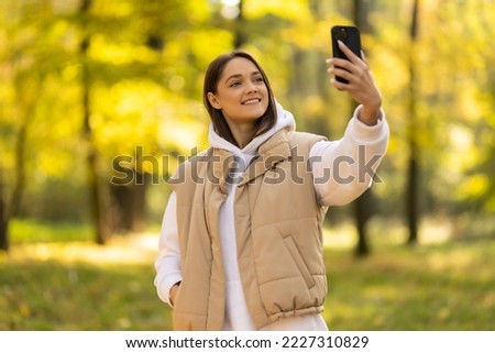 attractive young woman walking in autumn park taking selfie pictures with leaf using smartphone
