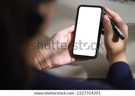 Mock up image of woman holding mobile phone while sitting at office desk. White empty screen for your advertise design.