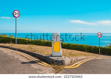 Road traffic speed signs at a junction against a bright blue sky and calm sea on a fine summer's day.