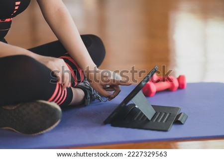 Crop picture. Hand's sportswoman touching on tablet sitting on yoga mat and doing exercise with dumbbell workout online and looking video streaming on tablet at fitness gym. Online fitness concept.