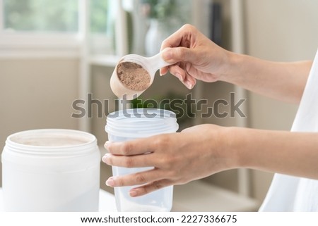 Diet meal replacement for weight loss, asian young woman in sportswear, hand in holding scoop making protein into bottle to shake, drink supplement for muscle after workout at home. Healthy body care. Royalty-Free Stock Photo #2227336675
