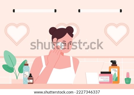 A girl is wiping her face with a cotton pad at the table with skincare products.