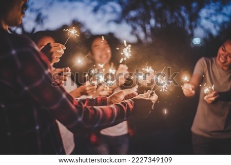 Group of young teenage friends stand in circle holding fire burning sparklers, They are raising and playing with sparkly in hands, Happy together in outdoor new year's party night