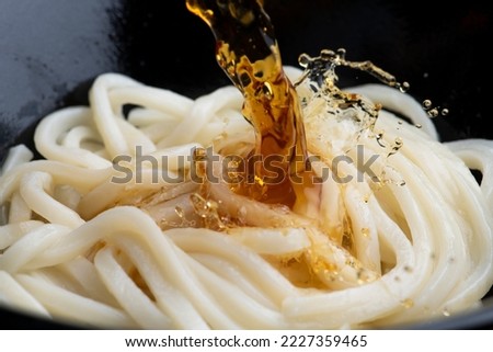 Cooking scene of pour soup stock over udon noodles.