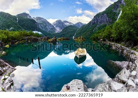 The boat is reflected in the clear water of the lake. The mountain lake Bondhuswatnet. Gorgeous Norway. Emerald green of summer grass. The picture was taken with a fisheye lens