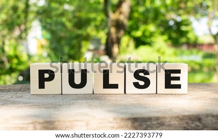 Five wooden blocks lie on a wooden table against the backdrop of a summer garden and create the word PULSE. Concept for your design