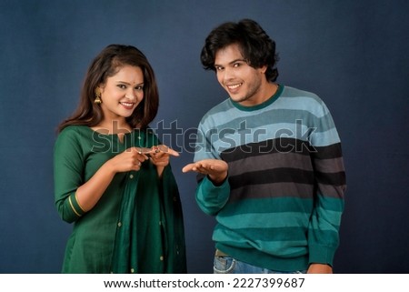 A young smiling happy couple standing together presenting something in their hand on a gray background. 