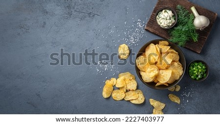 Crispy potato chips with herbs, salt and sour cream on a graphite background. Top view, copy space. Royalty-Free Stock Photo #2227403977