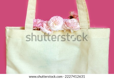 pink roses in eco textile shopping bag isolated on purple background.mini small flowers bouquet inside bag handles up free space for text mock up copy paste shopping consumerism sale discount money 