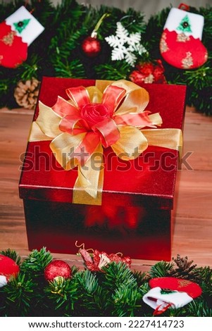 Gift box with gold color ribbon on wood background with Christmas tree and traditional ornaments Xmas props. Concept of happy and joyful in festival.