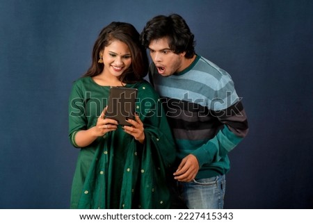 Happy young couple using mobile and showing a blank screen of a smartphone or mobile or tablet phone on a gray background 