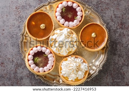 Festive set of sweetness tartlets with meringue and lemon curd, raspberry curd, nuts and chocolate close-up on a plate on the table. Horizontal top view from above
