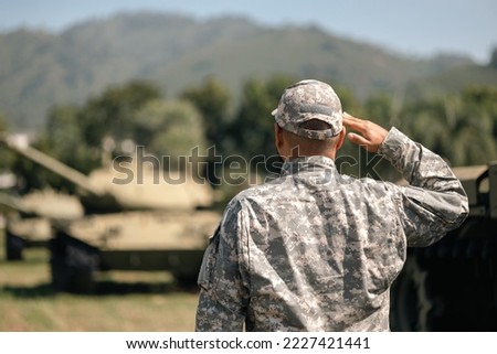 Asian man special forces soldier saluting standing against on the field Mission. Commander Army soldier military defender of the nation in uniform standing near battle tank while state of war.