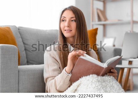Young woman with warm plaid reading book at home