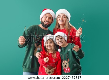 Happy family in Santa hats with Christmas sparklers on green background