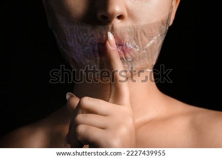 Young woman with taped mouth showing silence gesture on dark background, closeup. Censorship concept Royalty-Free Stock Photo #2227439955