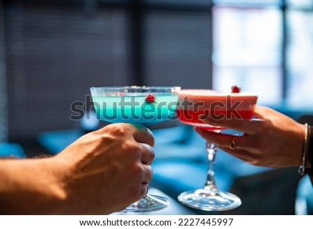 man and woman hand clinking glasses of alcoholic cocktails in bar