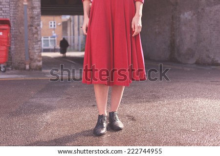 A young woman wearing a red dress is standing in the street