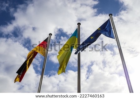 Flags of Ukraine, Germany and European Union fly side by side against blue sky