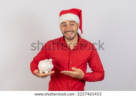 Handsome man in christmas hat holding a piggy bank on white background. End of year savings concept