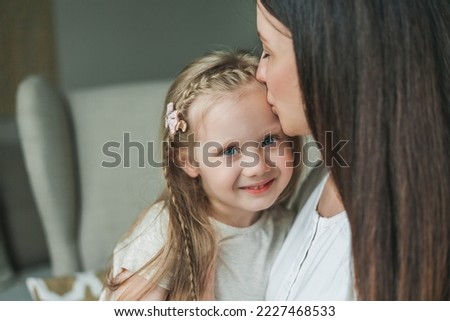 Cozy home portrait of a young beautiful dark-haired mother and her 4-year-old daughter with long shiny hair. Family relationships.