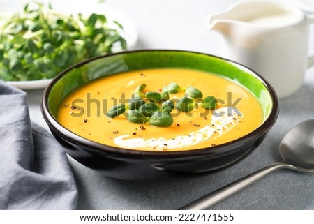 Creamy pumpkin fall soup in green bowl on the light gray table. Butternut squash cream soup garnished with heavy cream and fresh sunflower microgreen. Selective focus Royalty-Free Stock Photo #2227471555