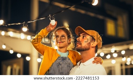 Happy Handsome Father Helping His Little Beautiful Daughter to Change a Lightbulb in Fairy Lights Backyard Installation at Home. Father and Daughter Repair Lights on a Porch. Royalty-Free Stock Photo #2227481153