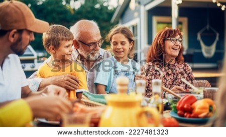 Portrait of a Happy Senior Grandfather Holding His Bright Talented Little Grandchildren on Lap at a Outdoors Dinner Party with Food and Drinks. Family Having a Picnic Together with Children. Royalty-Free Stock Photo #2227481323