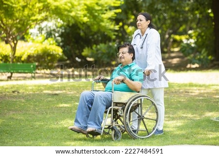 Indian caregiver nurse taking care of senior male patient in a wheelchair outdoor at park, Asian doctor help and support elderly mature older people. rehabilitation and health care. Royalty-Free Stock Photo #2227484591