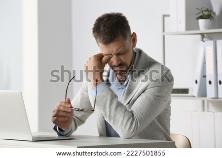 Man suffering from eyestrain at desk in office Royalty-Free Stock Photo #2227501855
