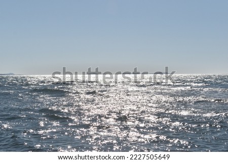 Sparkling sea in the horizon reflecting light rays from the sun on a clear sky day. Wallpaper, horizontal water photography.