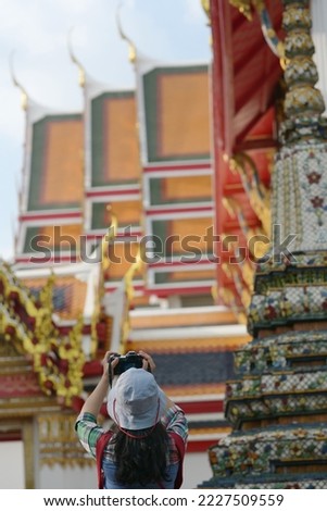 A woman uses a digital camera to capture the beauty of the churches and pagodas of famous Buddhist temples:Wat Pho or the Reclining Buddha Temple in Bangkok. Tourists wear light blue hats, green shirt