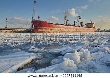 Cargo ship in the port in winter, against the background of ice, snow and blue sky during the day