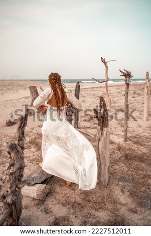 Model in boho style in a white long dress and silver jewelry on the beach. Her hair is braided, and there are many bracelets on her arms.