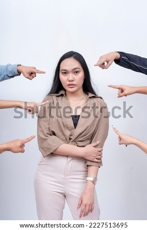 A sad and unnerved young woman being blamed. Arms from anonymous people pointing at her. Accusation and trial concept. Court of public opinion. Royalty-Free Stock Photo #2227513695