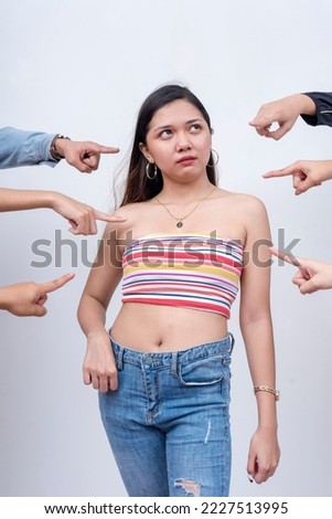 A young woman annoyed and irate from unfounded accusations. Arms from anonymous people pointing at her. Accusation and trial concept. Court of public opinion. Royalty-Free Stock Photo #2227513995