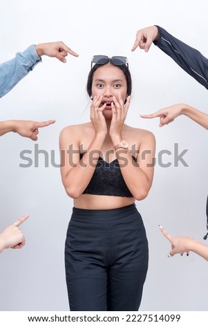 A shocked young woman in disbelief being blamed. Arms from anonymous people pointing at her. Accusation and trial concept. Court of public opinion. Royalty-Free Stock Photo #2227514099