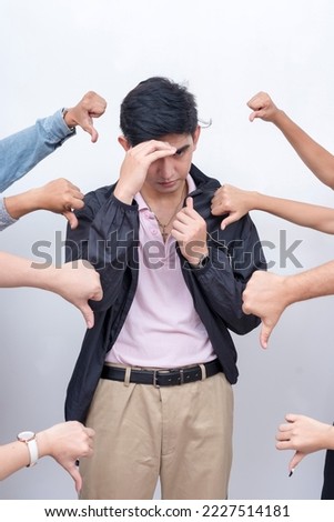 A young asian man shields himself from the criticism and scandals. Anonymous arms making a thumbs down sign giving negative feedback. Court of public opinion. Royalty-Free Stock Photo #2227514181