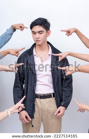 A sad and depressed young man being blamed. Arms from anonymous people pointing at him. Accusation and trial concept. Court of public opinion. Royalty-Free Stock Photo #2227514185