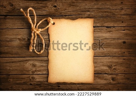 Paper label with old parchment texture, worn edges and a rope tied in the shape of a bow on a rustic brown wooden surface
