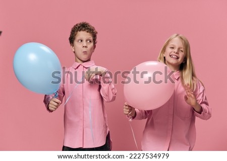 funny children, a boy and a girl are standing in pink clothes on a pink background and playing with inflatable balls. In the hands of the girl is pink, and the boy has blue balloons