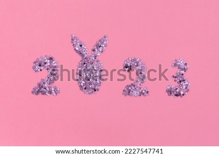 Date of New Year 2023 with symbol of year bunny rabbit ears shape from shiny pink sparkles on a pink background. Happy New Year holiday concept. Minimalism, creative flat lay, close up