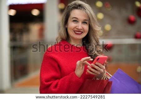 A woman shopping with a smartphone in a shopping mall, a happy girl talking on the phone in a shopping mall, holding shopping bags in her hands. High quality photo